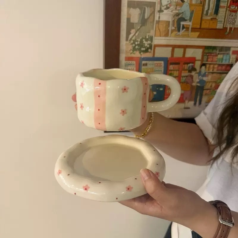 مج مع صحن عليه أزهار  صغيرة مرسومة يدويًا.